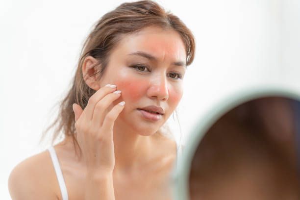 Woman examining her face in a mirror, focusing on her skin.